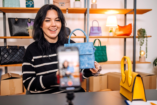 Young person begins new business with selling purses on line using internet and showing them to customer on mobile phone