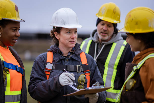 Labourers Planning on Site A small group of constructions workers huddle together as they take instructions from the site supervisor. They are each wearing proper protective gear and are listening attentively. overseeing stock pictures, royalty-free photos & images