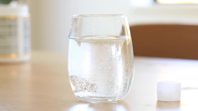 Slow video. White collagen powder dissolves in a transparent glass close-up.