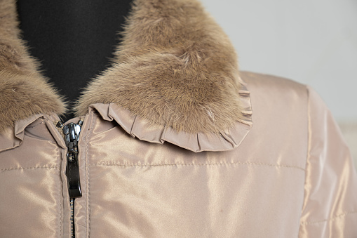 Fur collar on a warm women's beige jacket with zipper. Close-up of clothing detail.