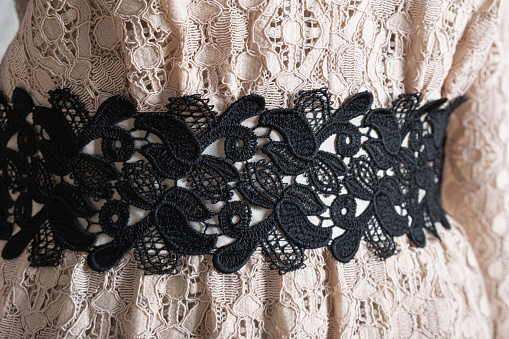 Close-up of a lace black belt on a beige dress. Romantic beige lace dress with black lace belt on a tailor's mannequin. Women's clothing in a seamstress's workshop.