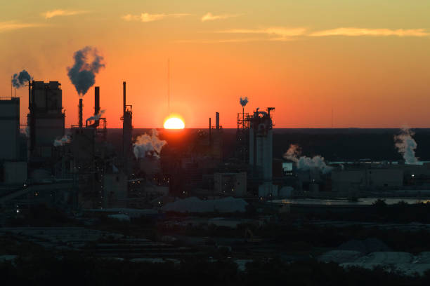 huge factory with high chimneys polluting atmosphere with carbon dioxide smoke from production process at plant manufacturing yard. industrial site at sunset - vapor trail night sky sunset - fotografias e filmes do acervo