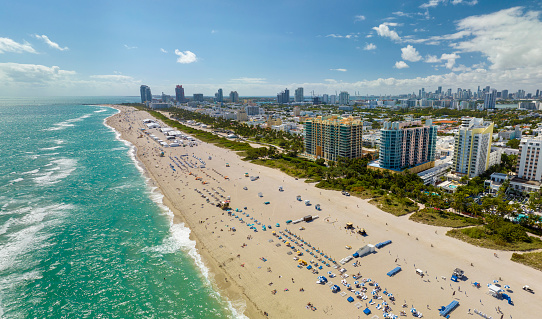 Travel destination in United States. South Beach sandy surface with tourists relaxing on hot Florida sun. Tourism infrastructure in southern USA. Miami Beach city with high luxury hotels and condos.