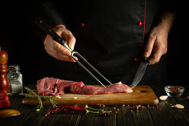 istock The cook prepares veal meat on the kitchen table before preparing a barbecue steak with aromatic spices. Fork and knife in the hands of a chef. 1917084535