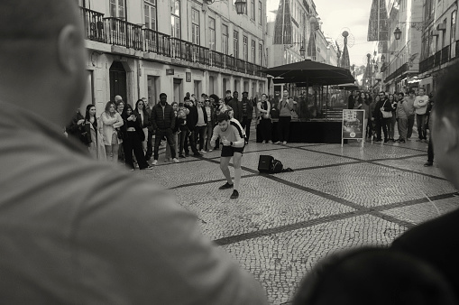 Lisbon, Portugal - November 1, 2023: A street artist performs a juggling act with a soccer ball at the Rua Augusta street in Lisbon downton.
