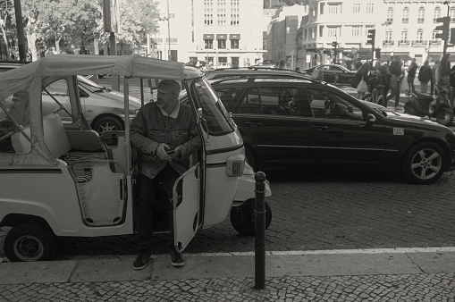 Lisbon, Portugal - November 1, 2023: A tuk-tuk driver waits for clients while sitting in his tuk-tuk in Lisbon downtown.