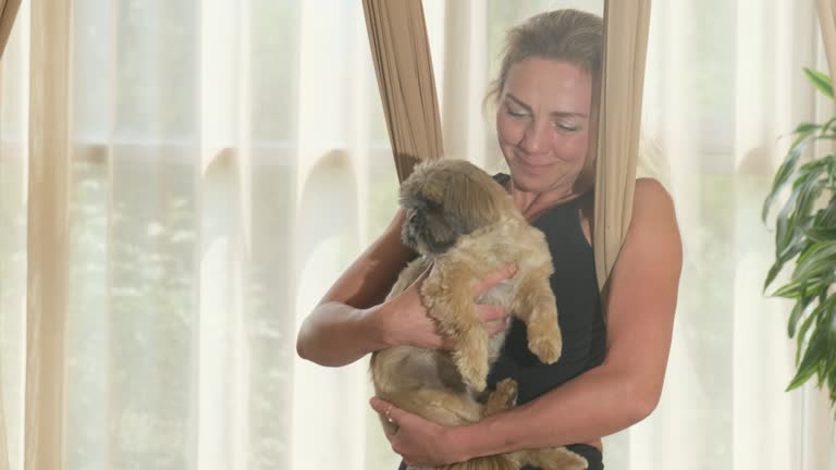 Woman stands with hammock fabric under armpits with dog