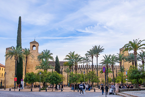 Groups of tourists are preparing to enter the Alcázar de los Reyes Cristianos in Cordoba, a medieval fortress located in the historic centre, whose construction was ordered by the King Alfonso XI of Castile in the year 1328. It is part of the Unesco World Heritage Site of Cordoba.