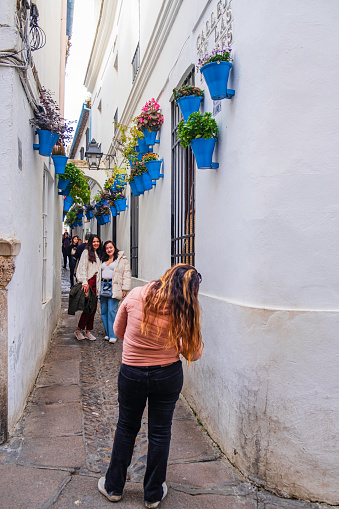 Young tourists taking picture in the charming Calleja de las Flores in Cordoba, a narrow alley in the old town where the blue flower pots hanging on the white walls create a suggestive setting.