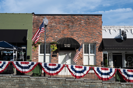 Fort Mill, South Carolina, United States - 11 Nov 2020: A snapshot of downtown Fort Mill captures the festive spirit as a brick building, hosting a hair salon, proudly displays 4th of July decorations.