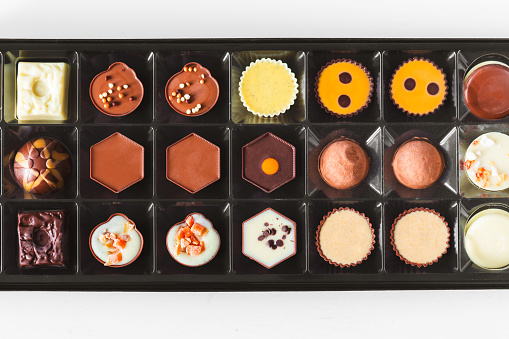 Close up color image depicting a box of gourmet chocolate truffles of different shapes and different varieties of chocolate. Selective focus with room for copy space.