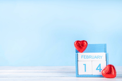 Valentine day celebration greeting card background with heart shape red chocolates and wooden calendar on February 14, on light blue background with copy space