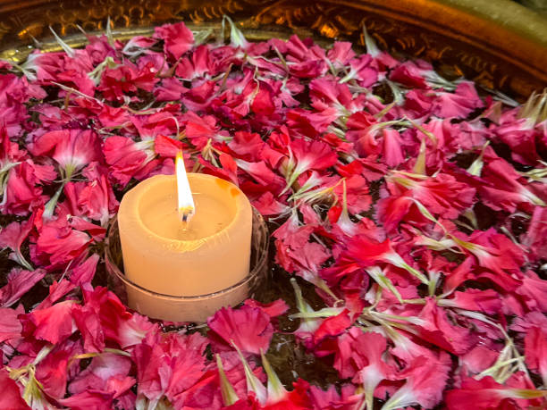 istock Full frame image of illuminated candle surrounded by dark pink carnation (Dianthus caryophyllus) petals floating in water, uruli / urli (metal water dish), traditional Indian home, hotel or temple welcome to guests, elevated view, focus on foreground 1917169288