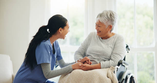 happy woman, doctor and holding hands with senior patient in wheelchair, support or trust for healthcare at home. medical nurse, caregiver or person with a disability smile for care or help at house - ouderenzorg stockfoto's en -beelden