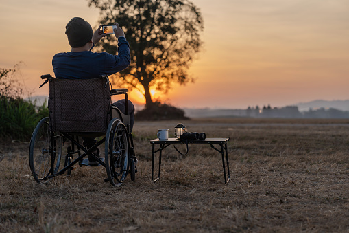 Man sitting on wheelchair with first golden sunrise of the day. Disabled handicapped people with hope.