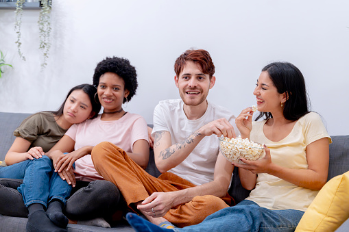 Group of friends sharing popcorn and enjoying leisure time together on a sofa.