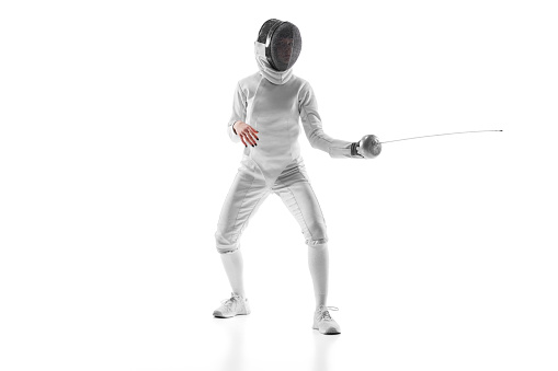 Female fencer intense gaze as she anticipates her opponent's move, tension palpable against white studio background. Concept of professional, sport active lifestyle, fitness, motion, strength.