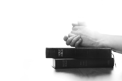 Christian silhouette praying and worshiping with hands on holy bible, religion, faith and belief background