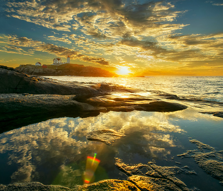 Magnificent landscape of a Nubble lighthouse at dawn. Reflection of the sky and clouds in the water between the rocks. USA. Maine. New England Seacoast. Panoramic photo.