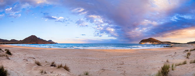 Panoramic image of white sand and turquoise waters underneath a bright blue sky with white puffy clouds in the Sea of Abaco in the Bahamas; landscape