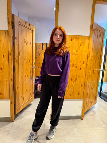 Stock photo showing a redheaded woman trying on a new purple cropped long-sleeved top in a department store changing room.