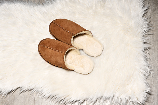 Brown warm slippers on white fur carpet