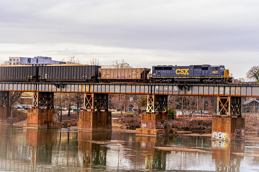Richmond, Virginia, USA - February 11, 2023 - A CSX Locomotive pulls a coal and freight train on the north bank of the James River as seen from the T. Pottersfield Bridge