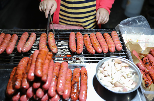 Grilling Meat on barbecue grill with hot coal. Grilled sausages are a common and affordable roadside snack in Taiwan. Sausage is made from ground pork. Taiwanese people like to eat raw garlic with sausage. \nSausages are carcinogens and are not recommended to be eaten too often.