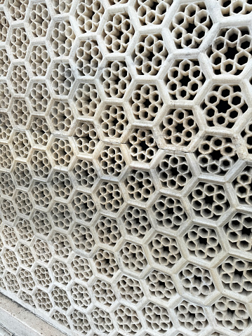 Stock photo showing close-up view of historic, ornate, Taj Mahal marble jali window screen architectural decoration. This honeycomb shaped design screen was designed for privacy and security whilst allowing light to enter a room as well as the free movement of air for ventilation.