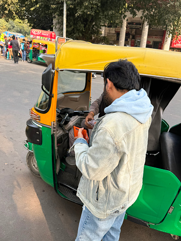 New Delhi, India - January 02, 2024: Stock photo showing parked auto rickshaw driver being paid by passenger at end of a ride.