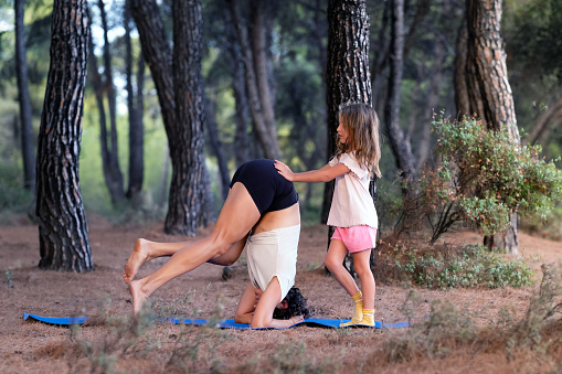 daughter helps mom stand on her head on a gymnastics mat in the forest