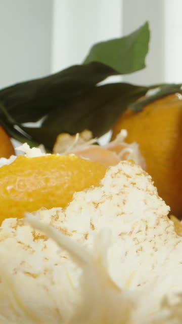 Vertical video. A man takes segments of a peeled mandarin from the table, among a large pile of fruits. Dolly slider extreme close-up.