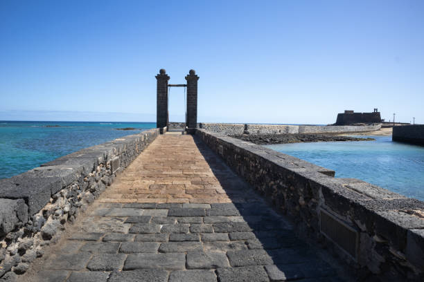 Stone bricks bridge in the Atlantic Ocean, to the Castle of Saint Gabriel (Castillo de San Gabriel). Calm water and horizon of the ocean. Castle in the background. Arrecife, Lanzarote, Canary Islands, Spain.