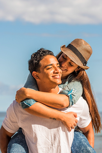 Young couple in love enjoy happiness and leisure activity - man carry woman in piggyback and smile with joyful - ocean water and blue sky in background - concept of summer vacation