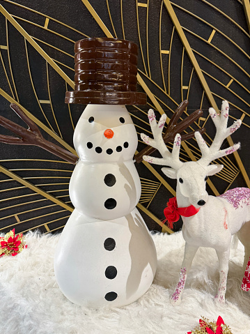 Stock photo showing close-up view of a 'Playful Snowman' ornament besides a model reindeer on artificial snow.