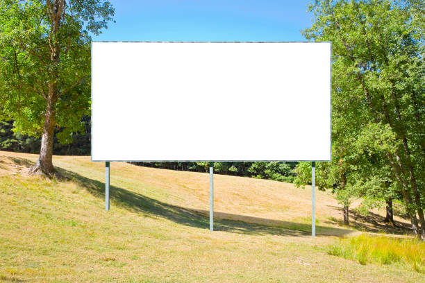 istock Blank advertising signboard in a green field with trees on background - concept with copy space for text inserting 1917404511