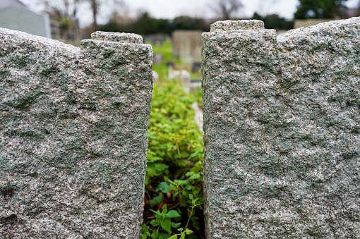 Shallow focus of a pair of granite gravestones showing a gap between to two graves. Distant vegetation can be seen.