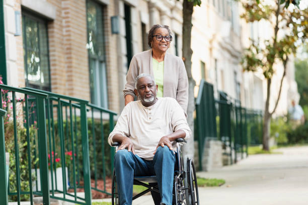 Senior woman pushing spouse in wheelchair on sidewalk