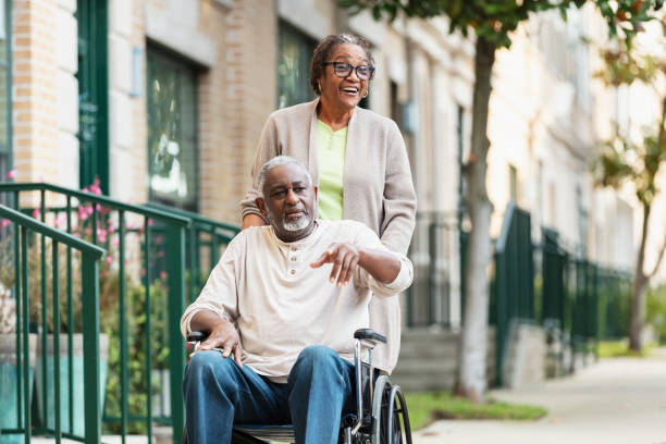 Senior woman pushing spouse in wheelchair on sidewalk