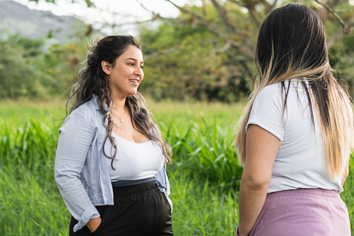 two young Latina women talking calmly, standing in the middle of a field of tall grass
