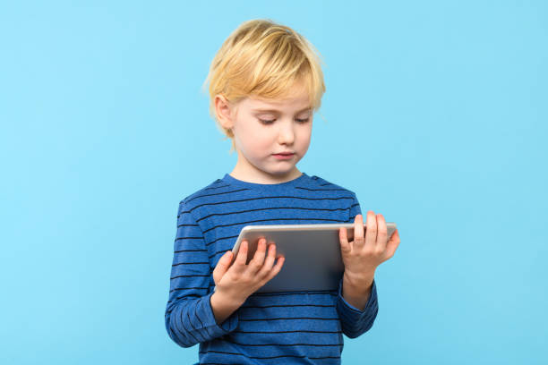 istock Young child holding digital tablet. Boy watching videos on his computer, isolated over pastel blue background. Children and technology. 1917436227