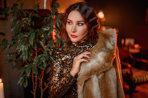 brunette woman wear fur coat and dress with sequins