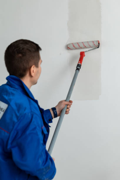 un lavoratore in giacca da lavoro blu applica la colla al muro con un rullo per tappezzare - paint roller copy space action adult foto e immagini stock