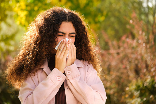 Young Caucasian woman with curly hair blowing your nose in a tissue at street in Autumn.