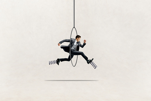 A businessman with springs on his shoes jumps through a hoop.