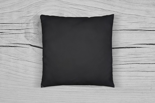 Black square throw pillow napping peacefully atop a rustic light gray wooden surface. Plenty of room for copy.