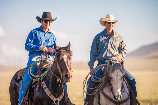A portrait of two young friends on horseback, enjoying working at a ranch during the summer.