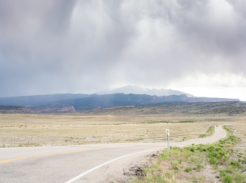 Storm clouds in the sky and rain falling on the distant mountains behind a desert highway in Utah, USA.
