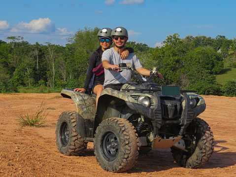 Happy young couple in nature on a quad bike. Young man and woman enjoying a quad ride in the countryside. Man driving and woman enjoying the ride with hands raised on a summer da