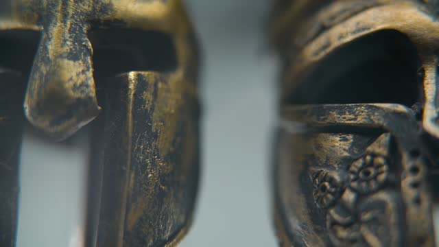 A close-up macro shot of a Spartan design, two different ancient warrior metal bronze helmets, textured shapes, studio lighting, Full HD cinematic video, hyper Slow Motion 120 fps, pan right
